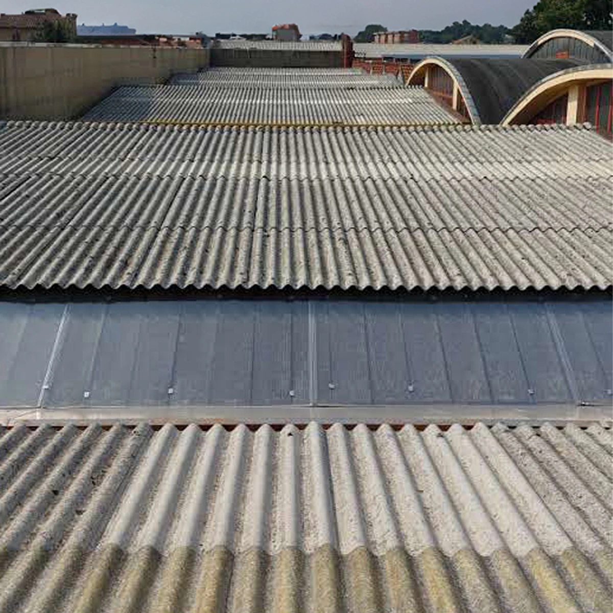 Coperture di capannoni industriali in lastre ondulate di cemento amianto, con una fascia di lucernari al centro della falda